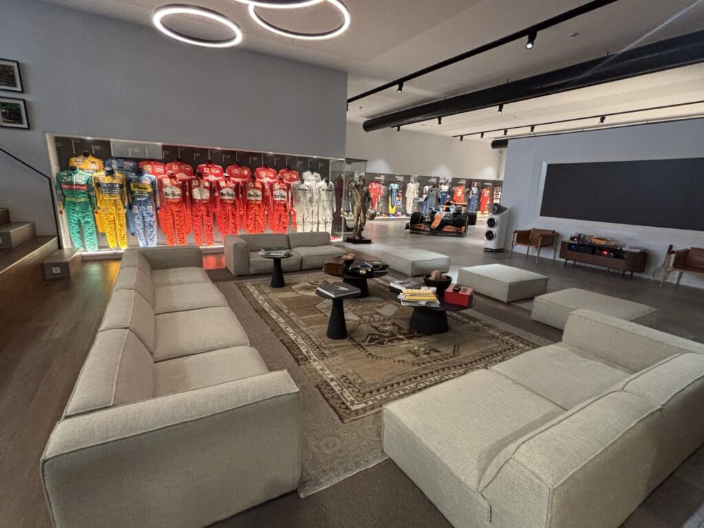 A living room with a huge sofa and a big screen, in the background Schumacher's race suits.