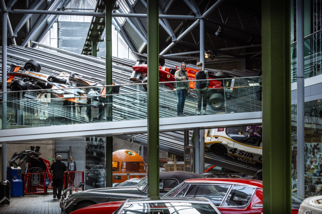 Racing cars in the background in front of people standing on a bridge.